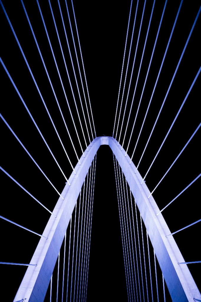 Looking up at a modern bridge structure with cables against a dark sky