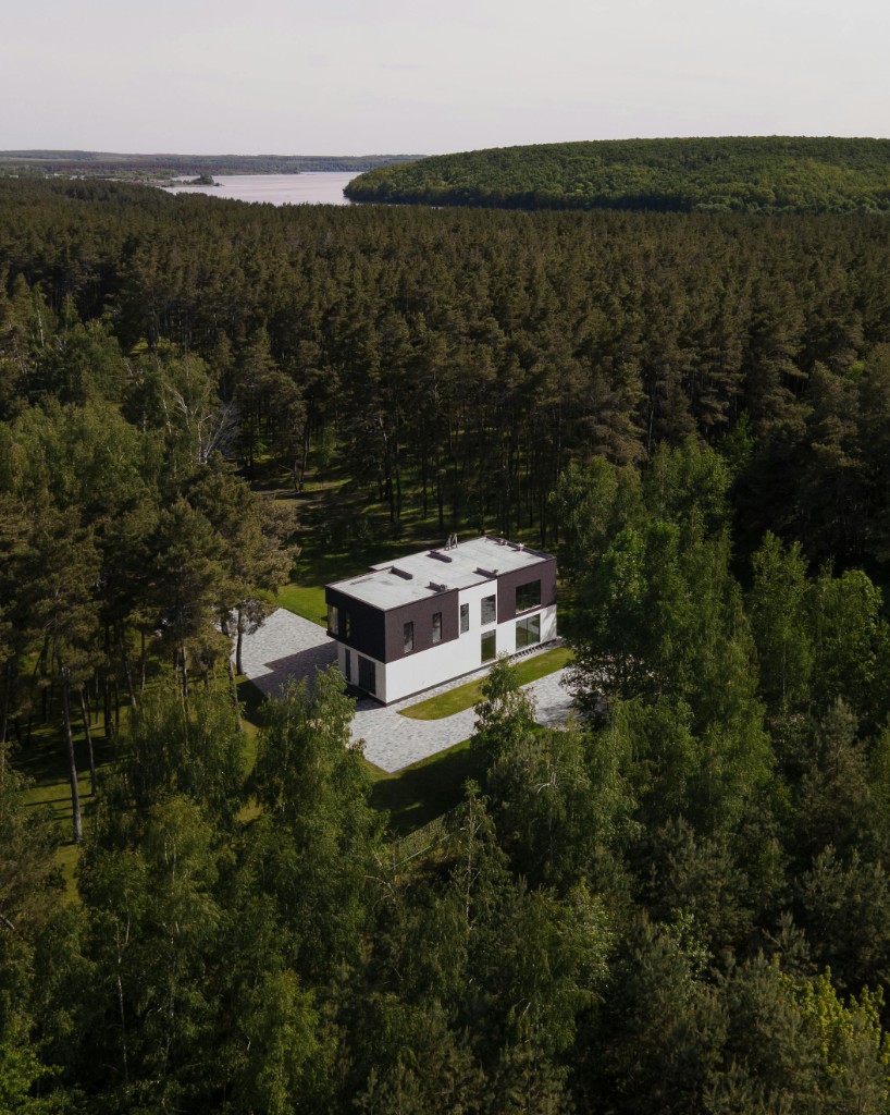 Aerial view of a modern home surrounded by forest near a lake