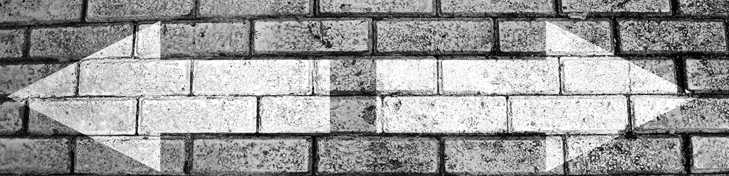 Brick wall with a white double-headed arrow painted horizontally across it