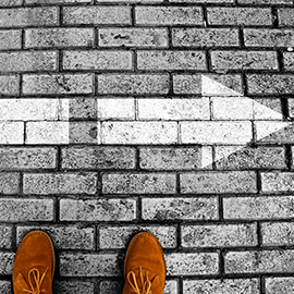 Brown shoes on brick pavement with a white arrow pointing right