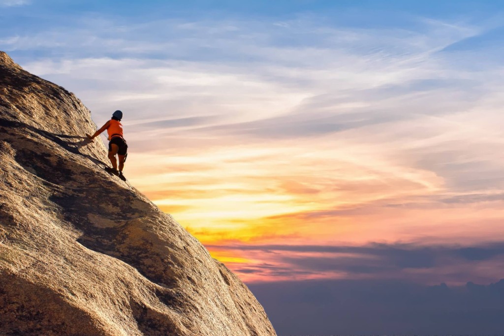 Rock climber ascending a steep mountain face at sunset