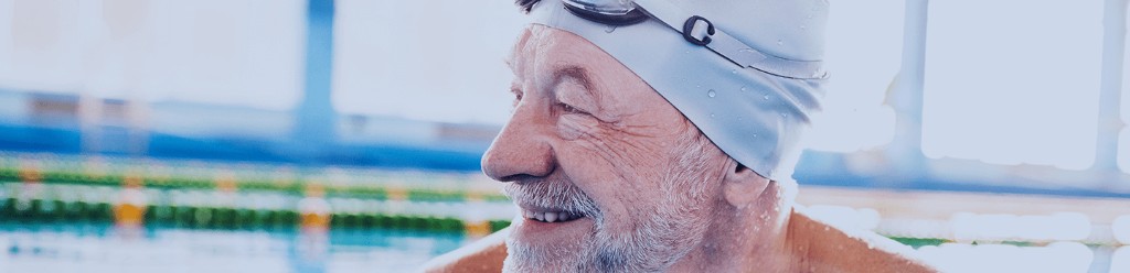 Older man smiling in a swimming pool wearing a grey swim cap