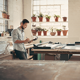 Man writing on a clipboard in a bright workshop with potted plants