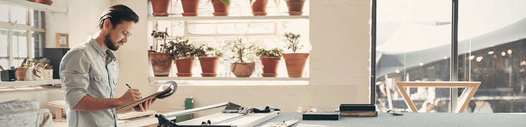 Man writing on a clipboard in a bright workshop with potted plants