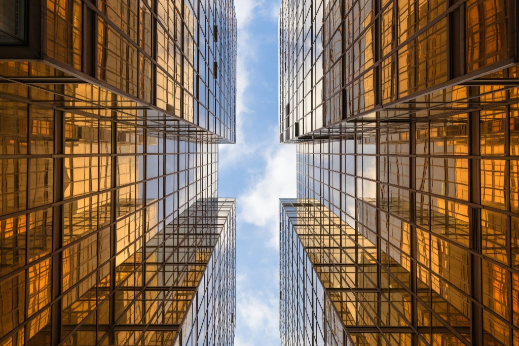 Looking up at four golden glass skyscrapers converging toward a blue sky