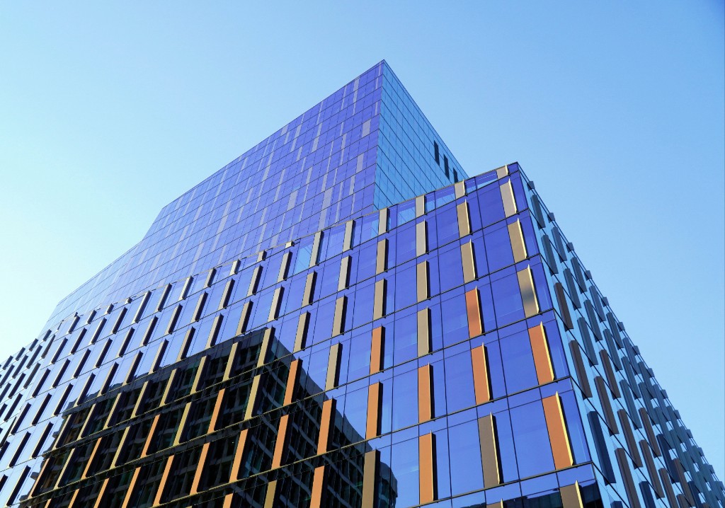 Looking up at a modern glass office building with copper vertical fins against a blue sky